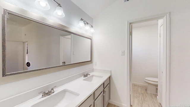 bathroom featuring wood-type flooring, large vanity, double sink, and toilet