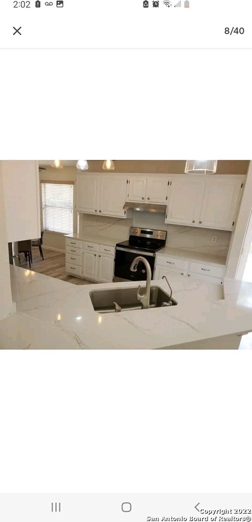 kitchen featuring light stone countertops, white cabinetry, sink, and stainless steel range with electric cooktop