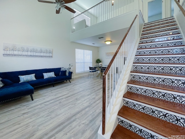 stairway with a towering ceiling, hardwood / wood-style flooring, and ceiling fan