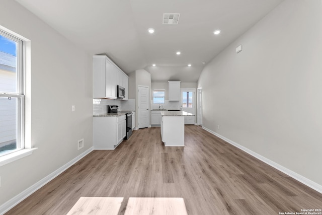 kitchen featuring white cabinetry, stainless steel appliances, light stone counters, vaulted ceiling, and decorative backsplash