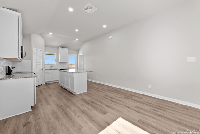 kitchen featuring a kitchen island, light stone counters, lofted ceiling, decorative backsplash, and white cabinets