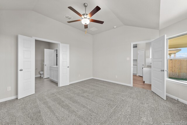 unfurnished bedroom featuring ceiling fan, light colored carpet, lofted ceiling, and ensuite bathroom