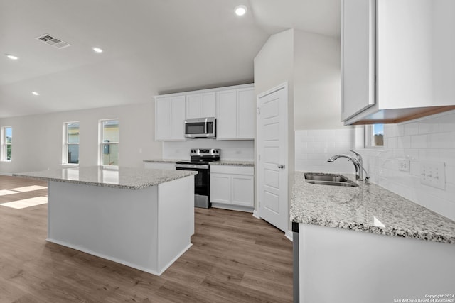 kitchen featuring white cabinets, sink, appliances with stainless steel finishes, a kitchen island, and light stone counters