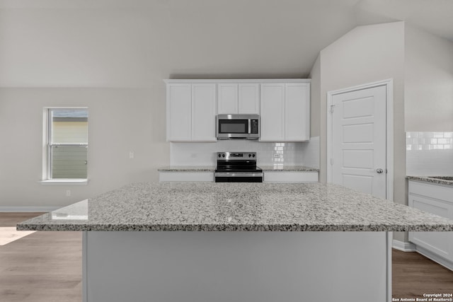 kitchen featuring a center island, vaulted ceiling, appliances with stainless steel finishes, tasteful backsplash, and white cabinetry