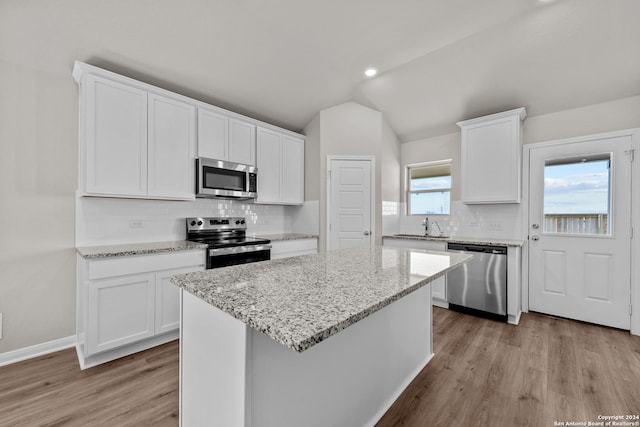 kitchen with white cabinets, a kitchen island, stainless steel appliances, and vaulted ceiling