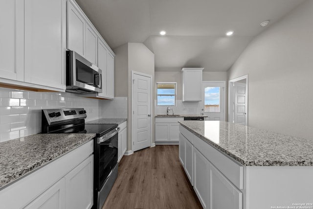 kitchen featuring stainless steel appliances, vaulted ceiling, sink, white cabinets, and a kitchen island