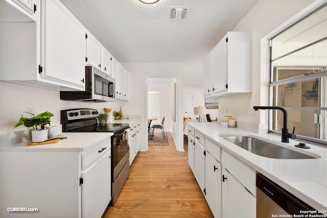 kitchen with light hardwood / wood-style floors, white cabinets, sink, a textured ceiling, and appliances with stainless steel finishes