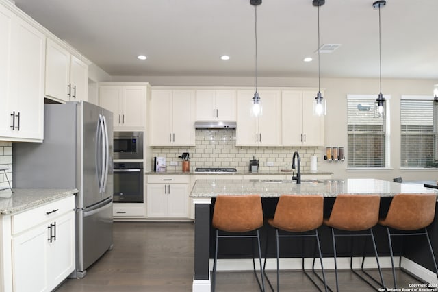 kitchen with light stone countertops, appliances with stainless steel finishes, pendant lighting, dark hardwood / wood-style floors, and white cabinetry