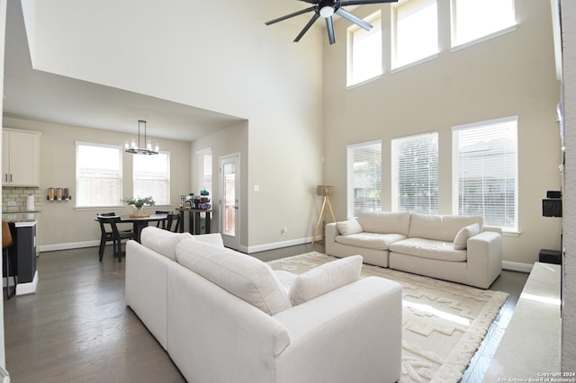 living room with plenty of natural light, a towering ceiling, wood-type flooring, and ceiling fan with notable chandelier