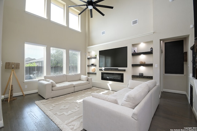 living room with a towering ceiling, dark hardwood / wood-style floors, built in features, and ceiling fan