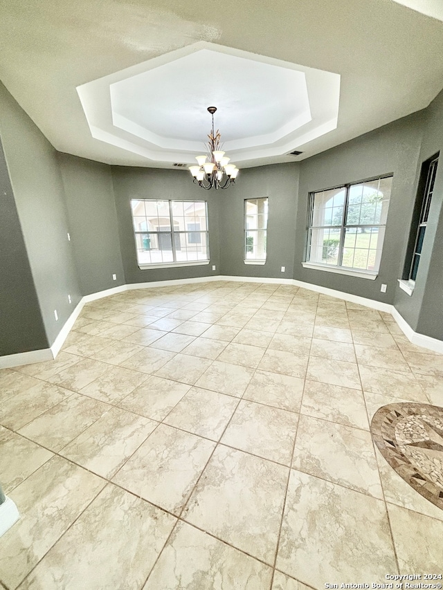 tiled empty room featuring a notable chandelier and a tray ceiling