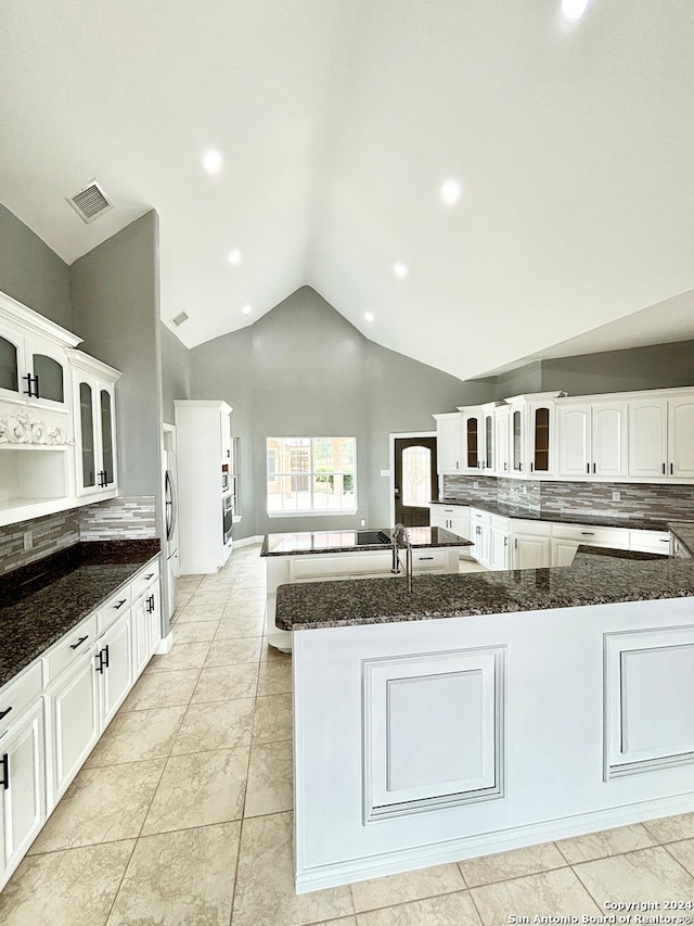 kitchen featuring a center island with sink, light tile patterned floors, white cabinets, and dark stone counters