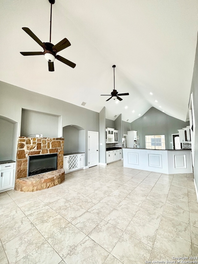 unfurnished living room with high vaulted ceiling, a stone fireplace, light tile patterned floors, and ceiling fan