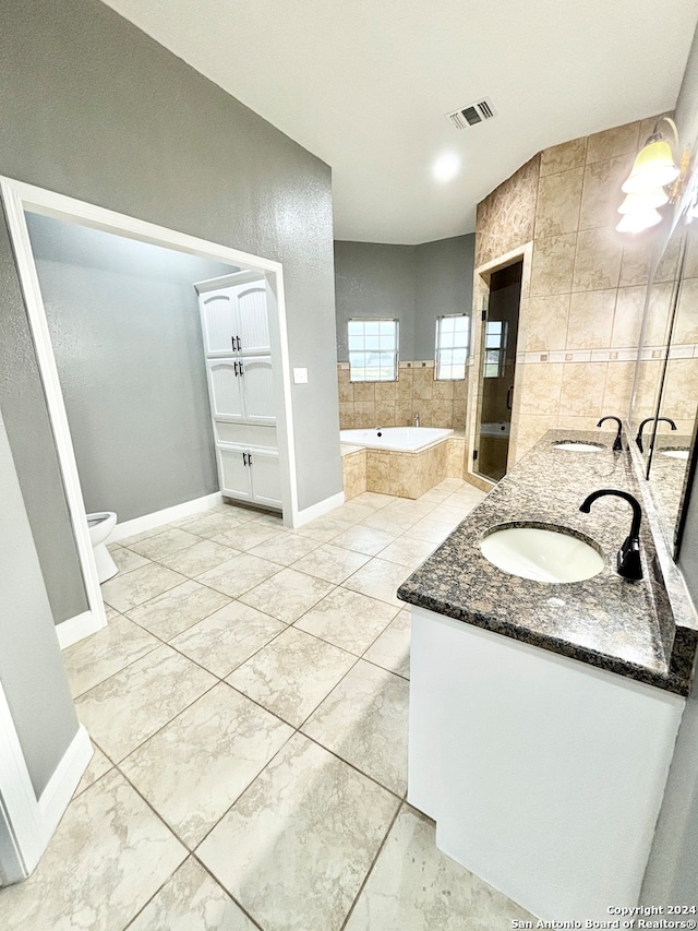 bathroom featuring toilet, tile walls, tile patterned flooring, tiled bath, and dual vanity