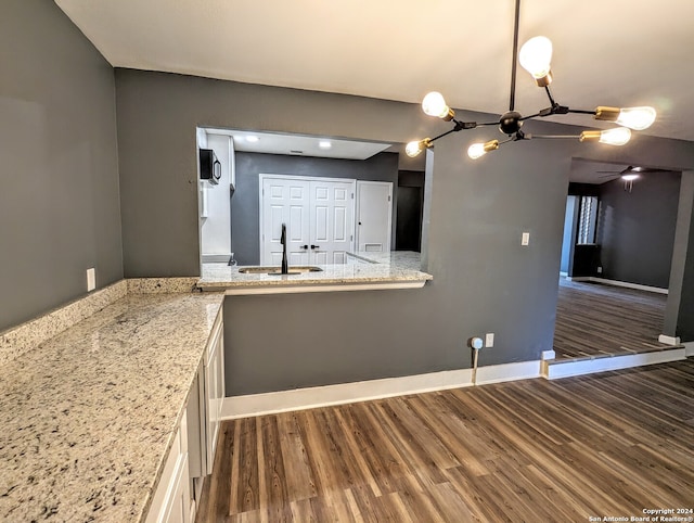 kitchen with light stone counters, dark hardwood / wood-style flooring, a notable chandelier, white cabinetry, and sink