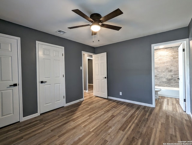 unfurnished bedroom featuring multiple closets, wood-type flooring, ensuite bath, and ceiling fan