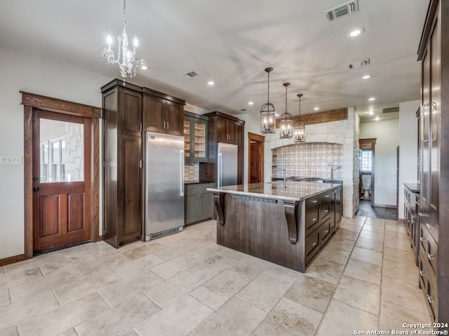 kitchen featuring an island with sink, tasteful backsplash, high end refrigerator, and pendant lighting