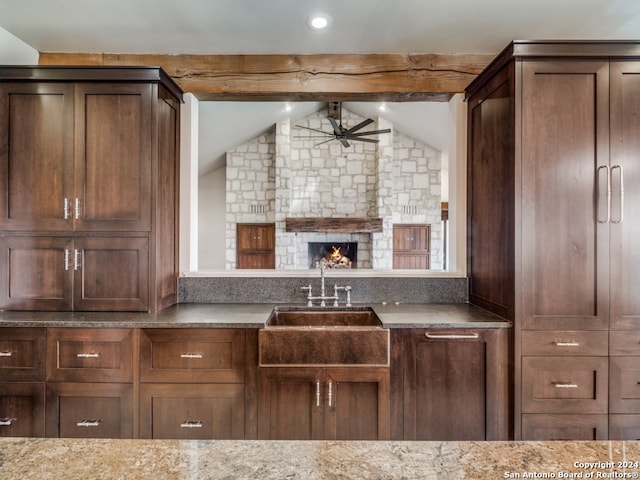 kitchen with sink, a stone fireplace, ceiling fan, and light stone countertops