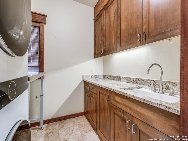 laundry area with sink, light tile flooring, stacked washer / drying machine, and cabinets