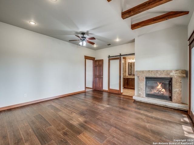 unfurnished living room with ceiling fan, dark hardwood / wood-style flooring, a barn door, and a high end fireplace