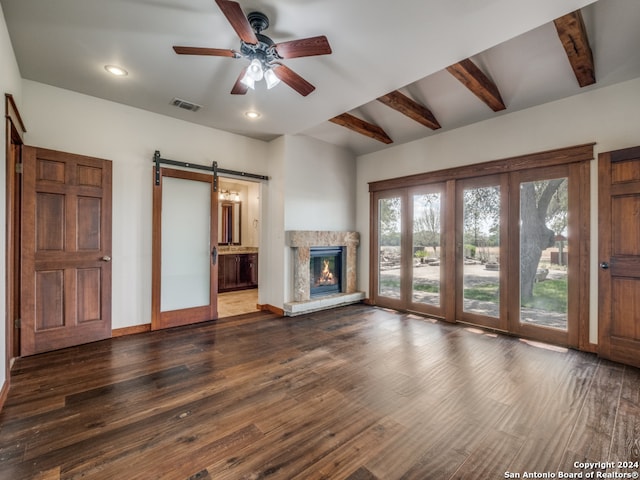 unfurnished living room featuring a barn door, dark wood-type flooring, ceiling fan, and lofted ceiling with beams