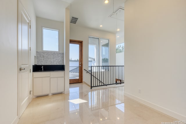 interior space featuring a healthy amount of sunlight, white cabinets, tasteful backsplash, and light tile floors