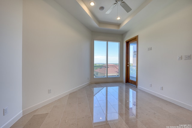 tiled spare room featuring ceiling fan and a tray ceiling