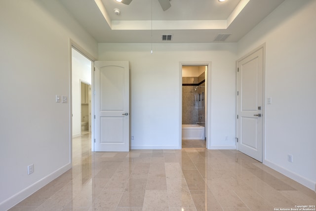 unfurnished bedroom featuring a tray ceiling, light tile flooring, and connected bathroom