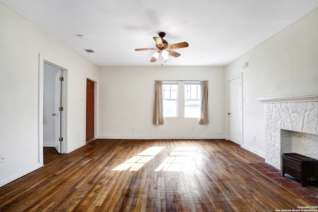 unfurnished living room featuring a stone fireplace, ceiling fan, and dark hardwood / wood-style floors