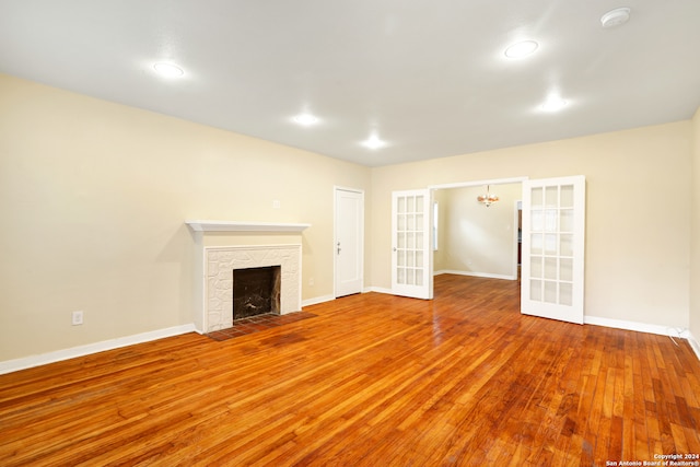 unfurnished living room featuring an inviting chandelier, a stone fireplace, and hardwood / wood-style flooring