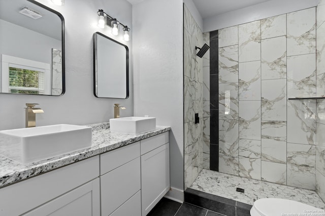 bathroom with a tile shower, dual bowl vanity, tile flooring, and toilet