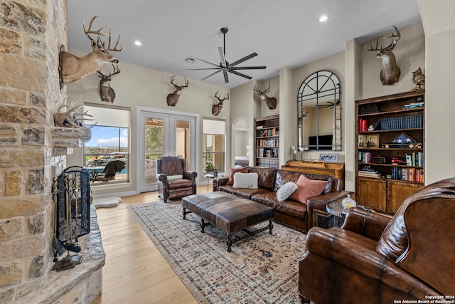 living room with ceiling fan, light hardwood / wood-style floors, french doors, a fireplace, and built in shelves