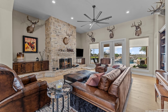 living room with ceiling fan, french doors, a fireplace, light wood-type flooring, and a towering ceiling