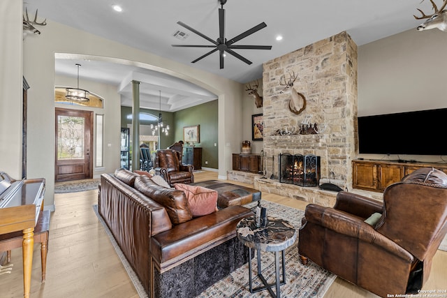 living room with high vaulted ceiling, a stone fireplace, light hardwood / wood-style floors, and ceiling fan with notable chandelier