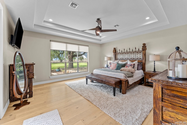 bedroom with a tray ceiling, light wood-type flooring, and ceiling fan