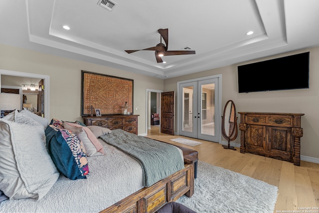 bedroom with a raised ceiling, french doors, and light hardwood / wood-style flooring