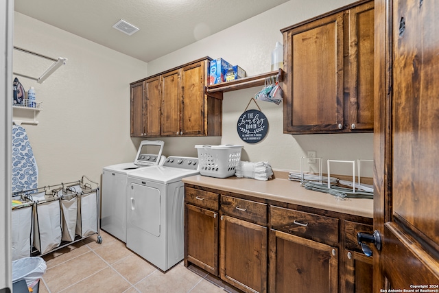 clothes washing area featuring cabinets, light tile floors, and washing machine and clothes dryer