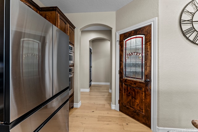 kitchen with dark brown cabinets, a textured ceiling, light wood-type flooring, and stainless steel refrigerator