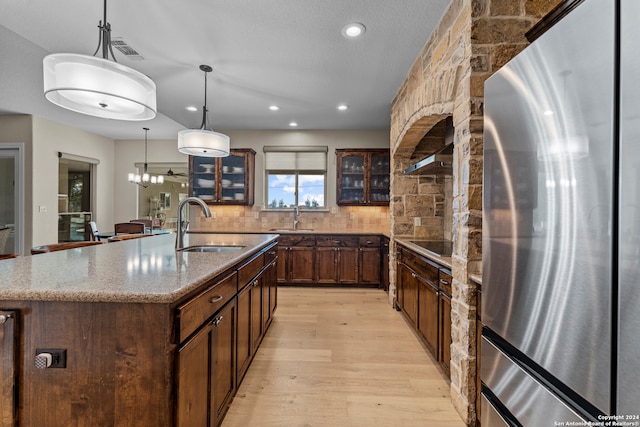 kitchen featuring stainless steel fridge, light wood-type flooring, a kitchen island with sink, sink, and tasteful backsplash