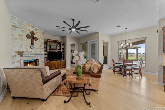 living room with wood-type flooring, a stone fireplace, a textured ceiling, and ceiling fan with notable chandelier