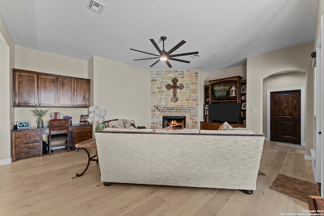 living room with a stone fireplace, ceiling fan, light hardwood / wood-style flooring, and a textured ceiling