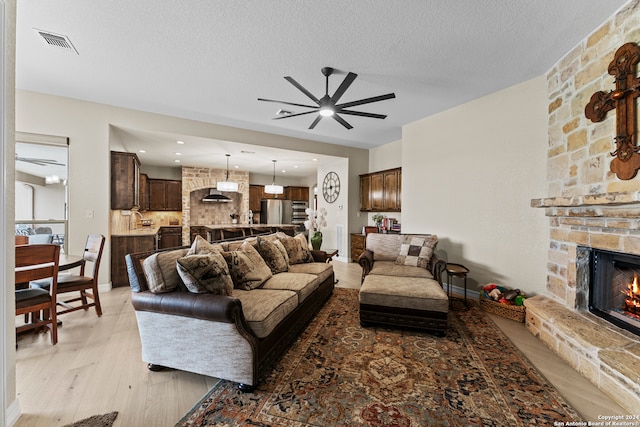 living room featuring a stone fireplace, ceiling fan, light wood-type flooring, a textured ceiling, and sink