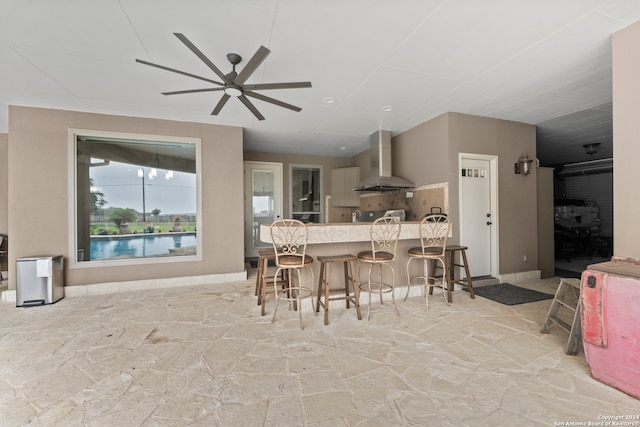 kitchen with stove, wall chimney exhaust hood, ceiling fan, and a breakfast bar