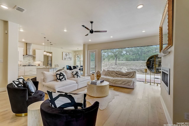 living room with sink, light wood-type flooring, and ceiling fan with notable chandelier