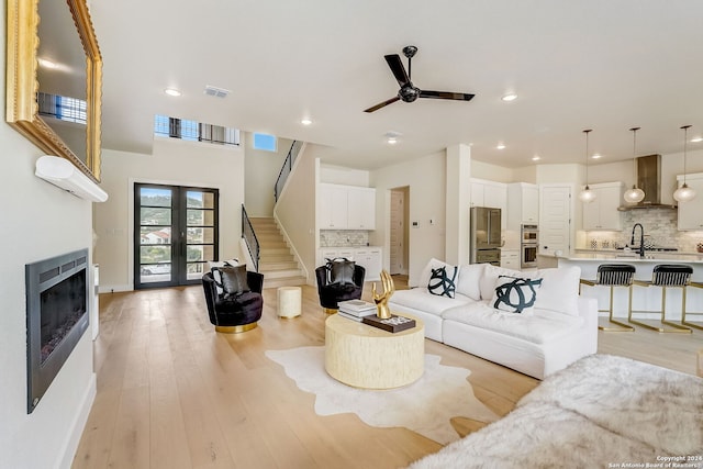 living room featuring ceiling fan, sink, french doors, and light wood-type flooring