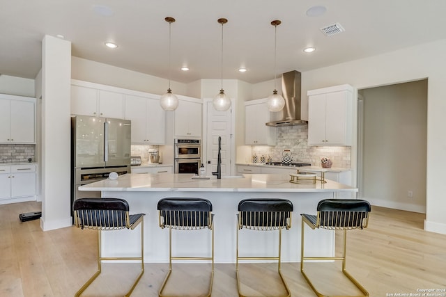 kitchen with backsplash, white cabinets, wall chimney exhaust hood, and light hardwood / wood-style floors