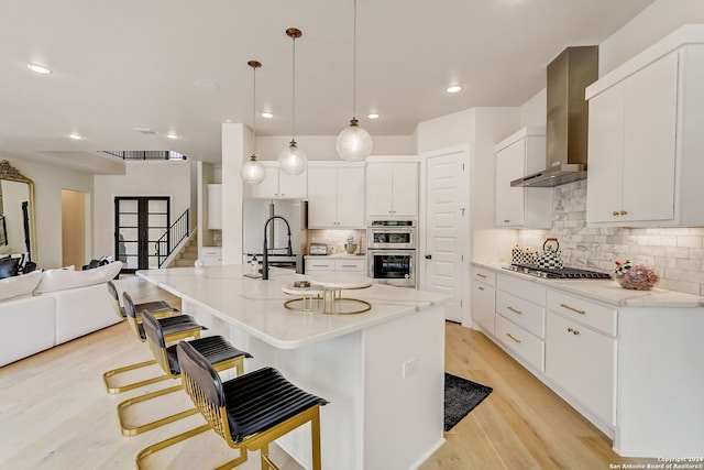 kitchen featuring wall chimney exhaust hood, light hardwood / wood-style floors, tasteful backsplash, and appliances with stainless steel finishes