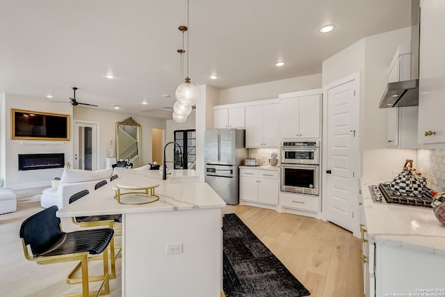 kitchen with light hardwood / wood-style floors, backsplash, stainless steel appliances, white cabinetry, and an island with sink