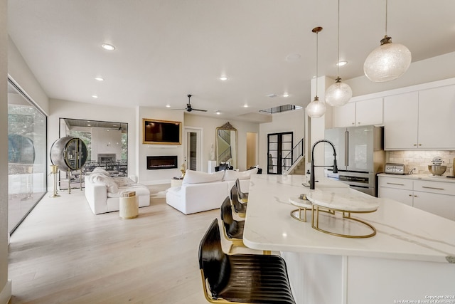 kitchen featuring tasteful backsplash, light wood-type flooring, a spacious island, hanging light fixtures, and white cabinets