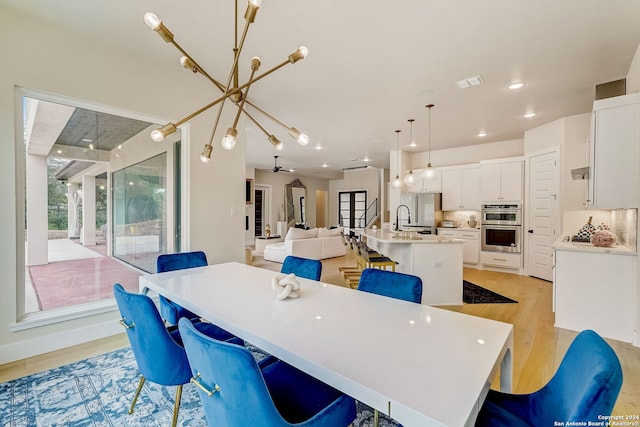 dining space featuring sink, light wood-type flooring, and an inviting chandelier